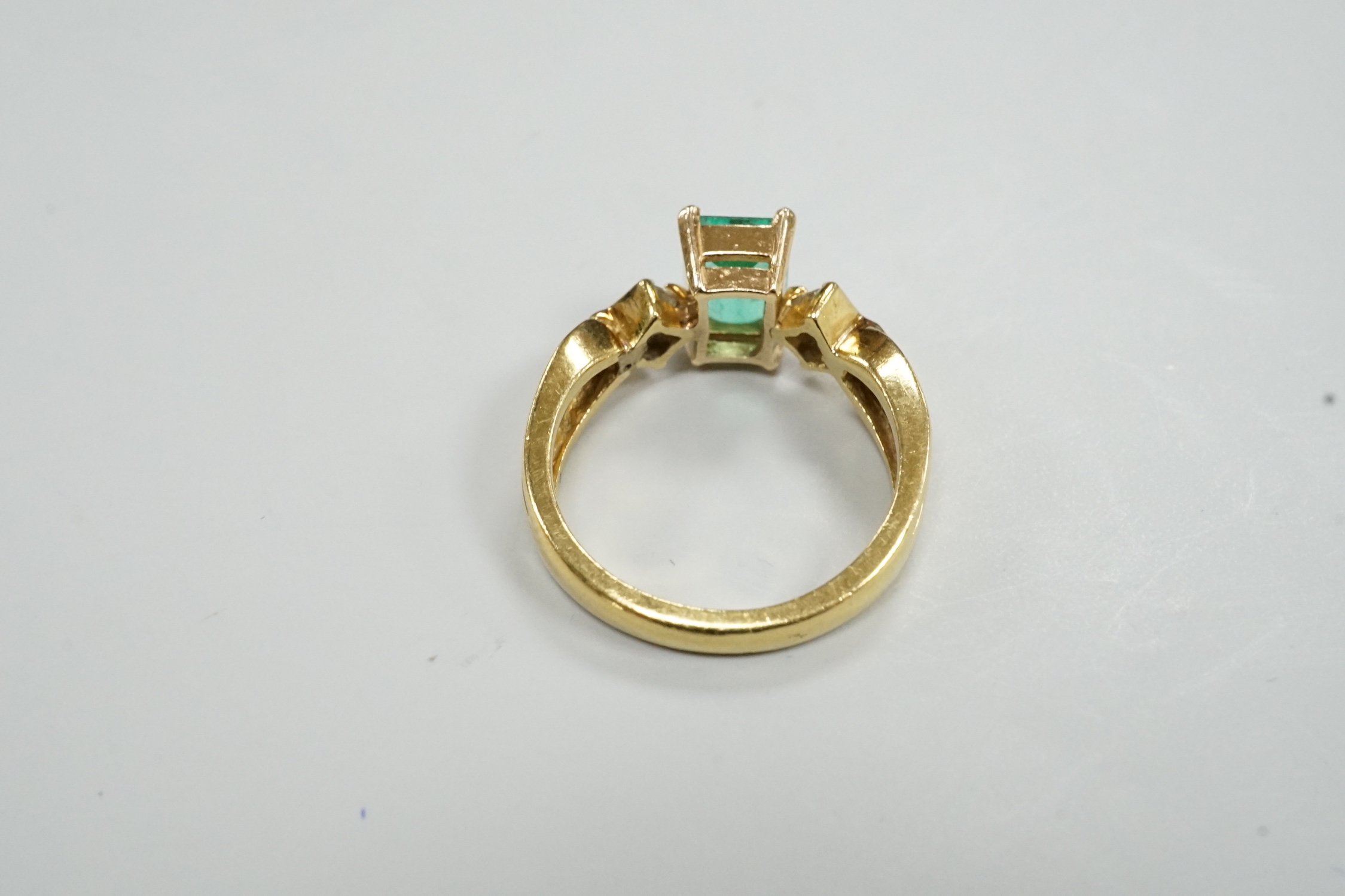 A modern 18k yellow metal and single stone emerald set ring, with two stone diamond set shoulders, size O, gross weight 5.8 grams.